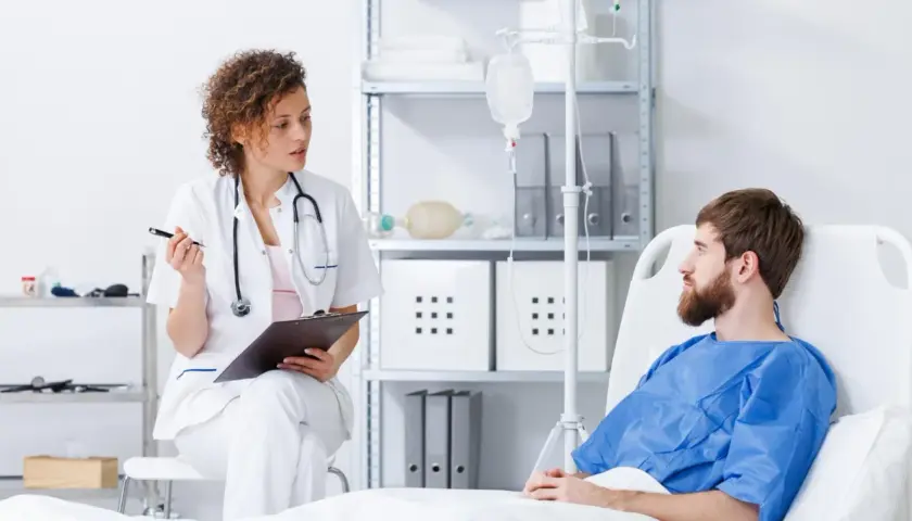 Lekarka rozmawia z pacjentem o jego leczeniu, w tym o możliwościach immunoterapii. W tle kroplówka i sprzęt medyczny.