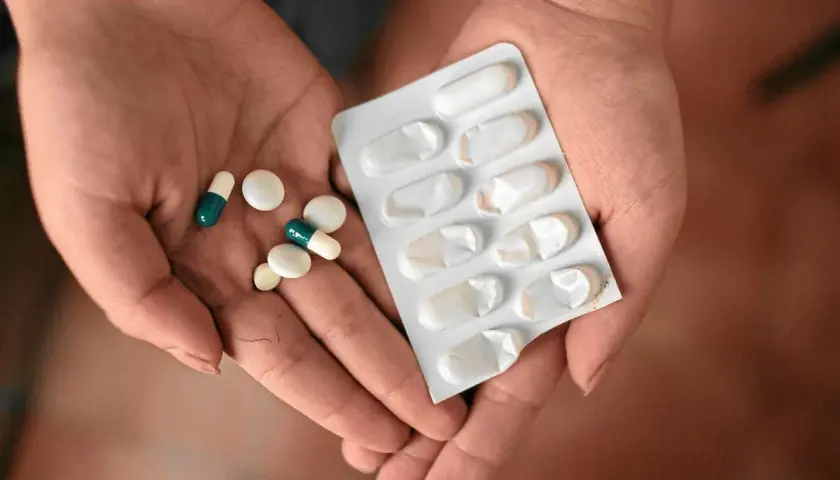 Dłonie trzymające tabletki i blister. Jedna z nich zawiera leki, które mogą być **inhibitory pompy protonowej**, stosowane w leczeniu problemów żołądkowych.