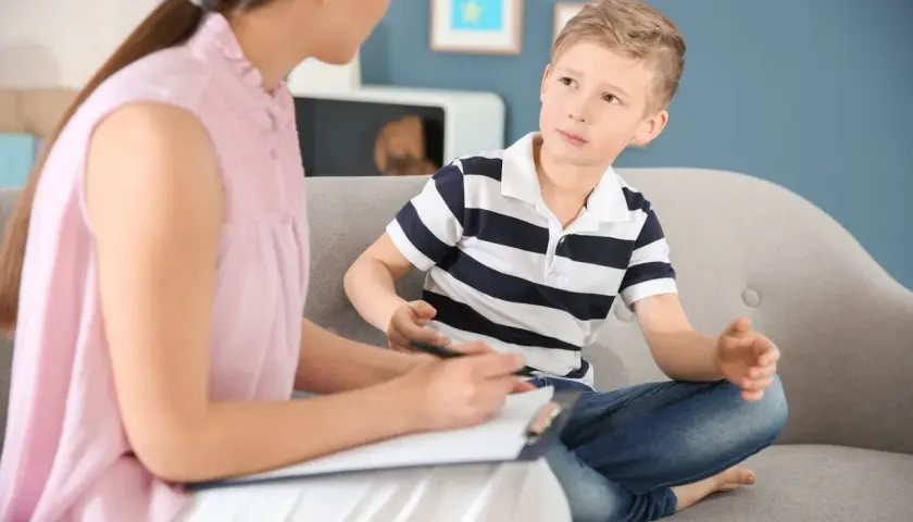 Psycholog rozmawia z chłopcem siedzącym na kanapie.