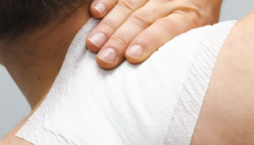 Dłoń uciska plaster przeciwbólowy na karku, przynosząc ulgę w bólu.